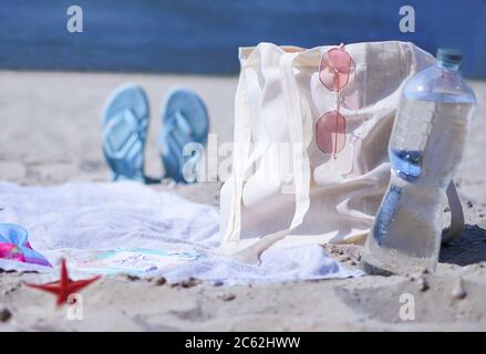A light eco bag stands on a caved shore, at a sledge, near a towel and things. They weigh glasses on a bag and a bottle of water is standing nearby. R Stock Photo