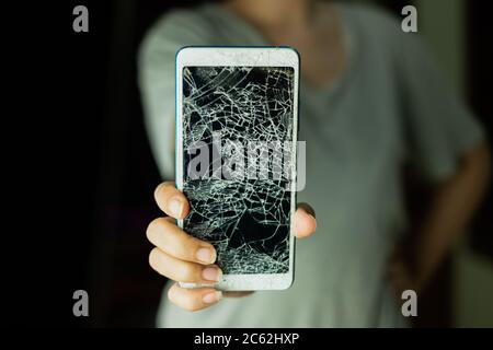 The woman standing and holding smartphone screen is cracked on black background Stock Photo
