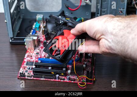 New PCU cooler in man hand over the disconnected motherboard near the case on brown surface. Close-up view Stock Photo