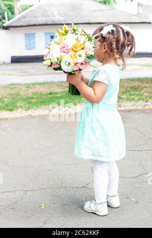 Little girl in beautiful dress holding the colorful wedding bouquet of flowers in hands. Wedding idea concept, close-up Stock Photo