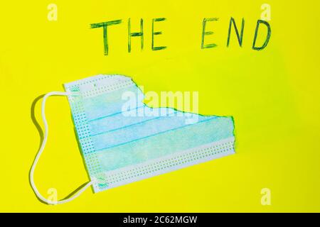 Surgical mask in a paper hole. COVID-19 protection Concept. Protective face mask and a torn yellow paper. Inscription 'The End'. Quarantine Completion Stock Photo