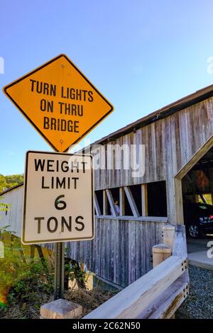 Classic US styled covered bridge seen next to an large orange sign warning drivers that one way traffic is permitted at one time. Stock Photo