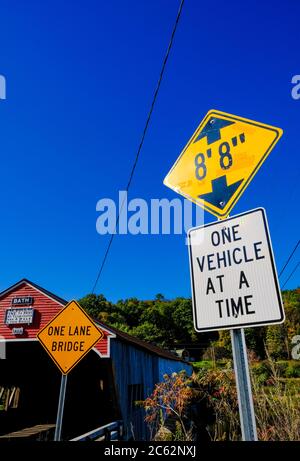 Classic US styled covered bridge seen next to an large orange sign warning drivers that one way traffic is permitted at one time. Stock Photo