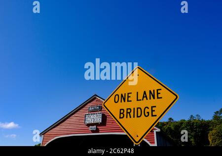 Classic US styled covered bridge seen next to an large orange sign warning drivers that one way traffic is permitted at one time. Stock Photo