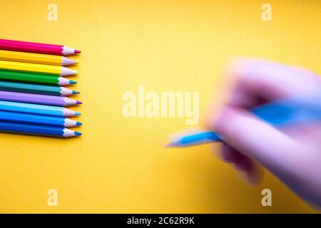 Colored pencils in a row in rainbow colors, hand with blue colored pencil draws on orange paper, retro background Stock Photo