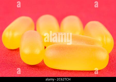 Macro shot of yellow gelatin capsules, isolated on a red background. Stock Photo