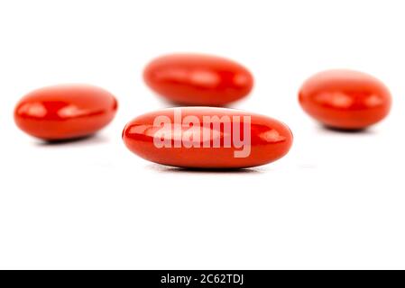 A macro shot of four red film-coated tablets arranged randomly, isolated on a white background. Stock Photo