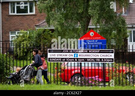 People walk past a sign outside a church advertising an online worship live stream, July 2020. Stock Photo
