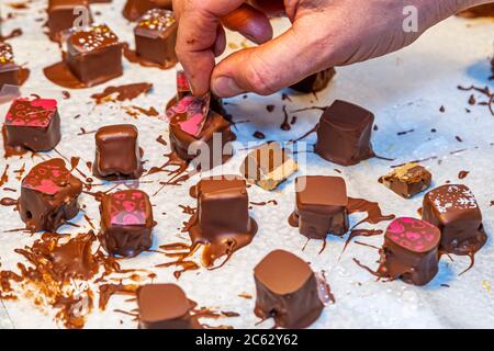 A participant places edible transfer sheets patterned with hearts and roses onto freshly coated pralines at the chocolate truffle workshop "Peter sei selig – Genusspunkt Küche" in Grevenbroich, Germany. A bitten piece reveals a pale caramel-nougat filling. Stock Photo