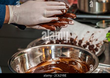 Wearing disposable gloves, a participant shapes truffle balls from melted chocolate at the chocolate truffle workshop "Peter sei selig – Genusspunkt Küche" in Grevenbroich, Germany. Finished balls already lie ready on baking paper beside the mixing bowl. Stock Photo
