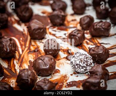 Among dark chocolate truffles at the chocolate truffle workshop "Peter sei selig – Genusspunkt Küche" in Grevenbroich, Germany, one pale ball is coated in white powder. Streaks of chocolate trail across the baking paper. Stock Photo
