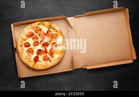 Pizza in a cardboard box on a dark chalkboard. Space for your text. Top view of pizza package. Pizza delivery. Stock Photo