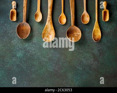 Various wooden spoons on dark green. Top view of kitchen utensils. Stock Photo