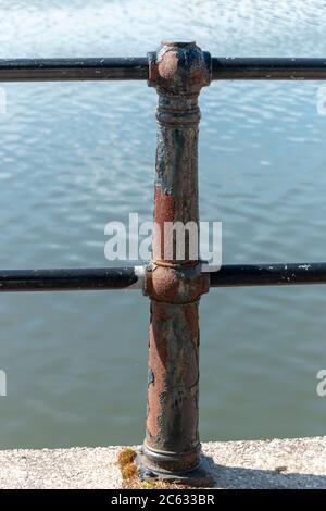 a close up view of a rusted metal fence pole that is located on the edge of the water at the harbour Stock Photo