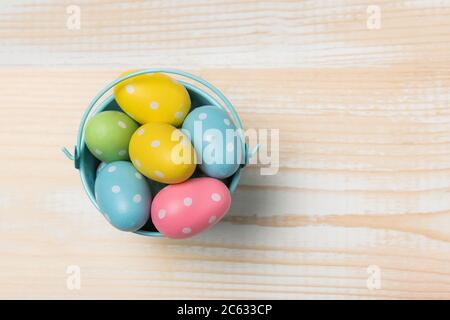 Colored bright Easter eggs in a bucket. Light wooden background. Copy space, top view. Stock Photo