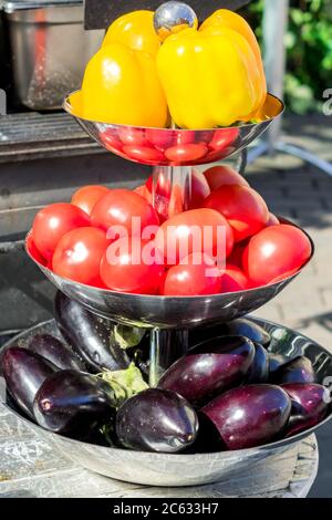 yellow bell peppers, red tomatoes and purple eggplants on metal three metal bowl outdoors Stock Photo