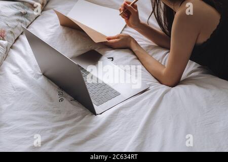 Young woman lies on bed with laptop and notebook. Stock Photo