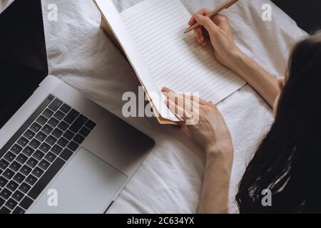 Young woman lies on bed with laptop and notebook. Stock Photo