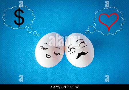 Faces on the easter eggs, money vs. love concept with heart and dollar sign on blue background Stock Photo
