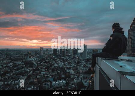 Circa June 2018: Person Sitting on Rooftop edge overlooking Cityscape of Frankfurt am Main, Germany Skyline at Night with City Lights Stock Photo
