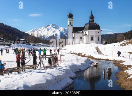 Seefeld, Tirol, Austria - 8 March 2020: Cross-country skiers on sunny track along a river and a pitoresque church Stock Photo