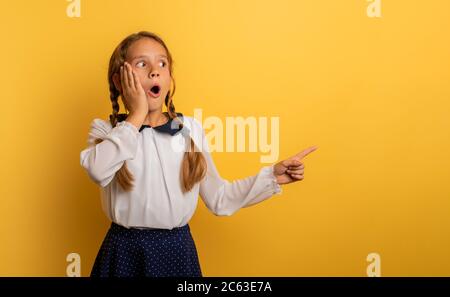 Young student is with shocked expression and indicates something. Yellow background Stock Photo