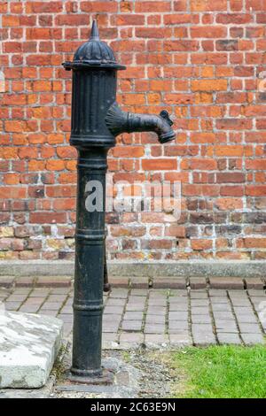 Antique cast iron water pump against a red-brick wall backgound Stock Photo