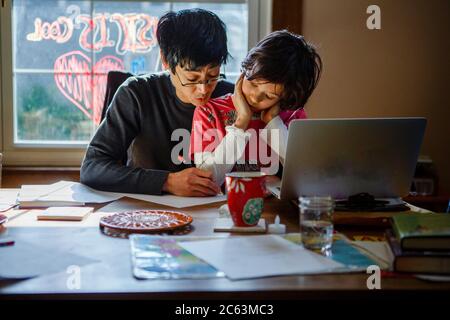 A father works home at the dining room table with his son in his lap Stock Photo