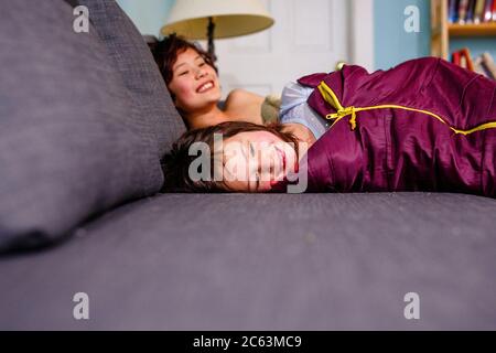 two happy smiling children lay together on a couch in sleeping bags Stock Photo