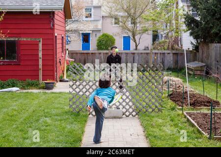 A boy and his father play makeshift tennis in yard over wood fencing Stock Photo