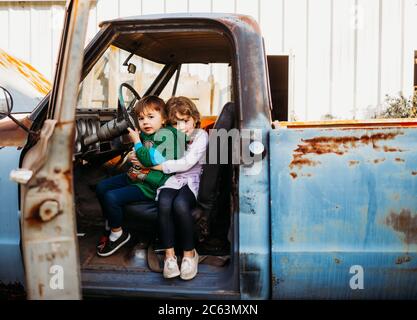 Young brother and sister sitting and hugging in vintage truck Stock Photo