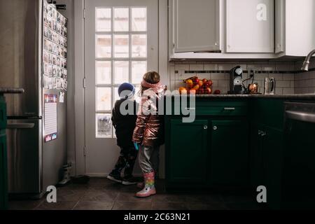 Young brother and sister wearing jackets waiting to go outside Stock Photo