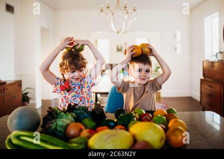 Young boy and girl sitting at kitchen counter playing with fruit Stock Photo