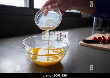 Pouring milk into egg batter, sliced tomatoes in background. Stock Photo