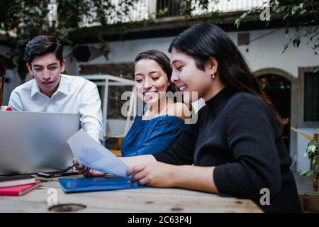 Young latin woman working with computer and her coworkers at the office or coworking in Mexico or South America, Mexican teamwork Stock Photo