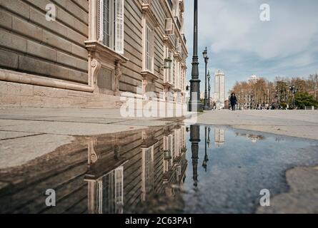 Ground level of stone sidewalk with aged building reflecting in water of puddle on sunny day in Madrid Stock Photo