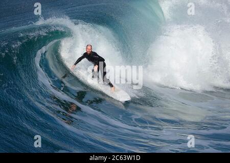 Older male surfer riding a large, beautifully curling wave Stock Photo