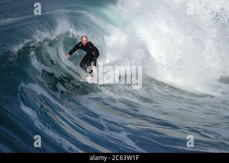 Older male surfer riding a large, beautifully curling wave Stock Photo