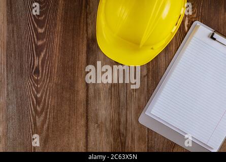Engineer working on office desk with blank notebook construction protective yellow safety helmet on wood table Stock Photo