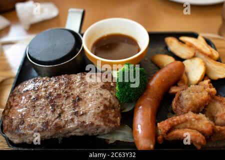 Pork steak with sausage and fried chicken and french fries on a black hot pan placed on the table in a Japanese restaurant Stock Photo