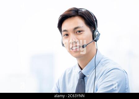Friendly smiling Asian male telemarketing operator wearing microphone headsets ready to service Stock Photo
