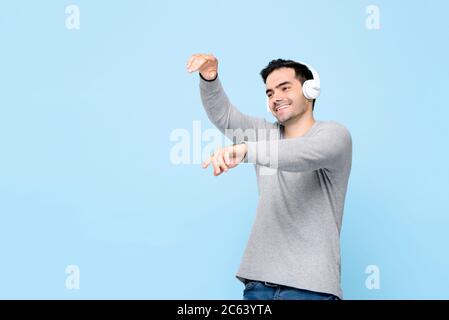 Happy Caucasian man listening to music from headphones and dancing on isolated studio light blue background Stock Photo