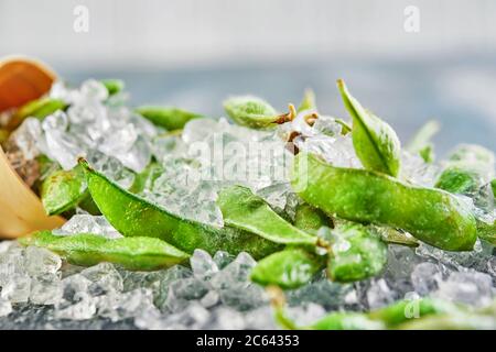 Frozen Edamame or soybeans in the mix with crushed ice on a blue background. Stock Photo