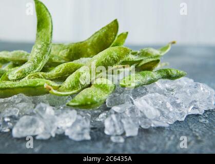 Frozen Edamame or soybeans in the mix with crushed ice on a blue background. Stock Photo