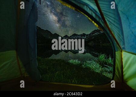 The Milky Way and its reflection can be seen through a tent door rising over the mountains Stock Photo