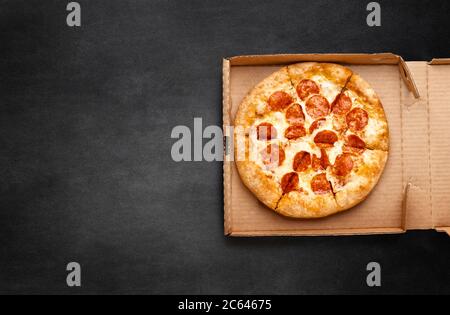 Pizza in a cardboard box on a dark chalkboard. Space for your text. Top view of pizza package. Pizza delivery. Stock Photo