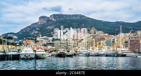 line up of luxury yachts at Port Hercules against the backdrop of the Tête de Chien (Dog's Head) rock promontory towering over Monaco, Principality of Stock Photo