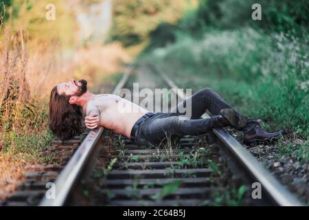 sad bearded young man lying on a railroad track Stock Photo