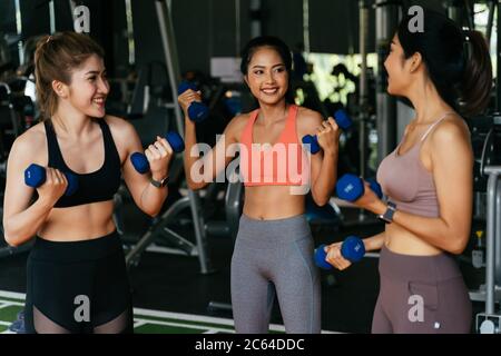 Happy young multiracial team of female athletes in sportswear training together with dumbbells in fitness club Stock Photo