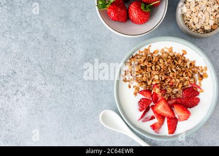 Greek yogurt with granola and strawberries in a bowl on concrete table. Top view, copy space for text or design. Concept of clean eating, dieting Stock Photo